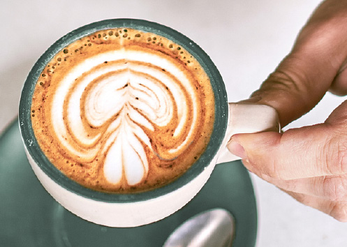 a hand holding a well-crafted latte in a green mug