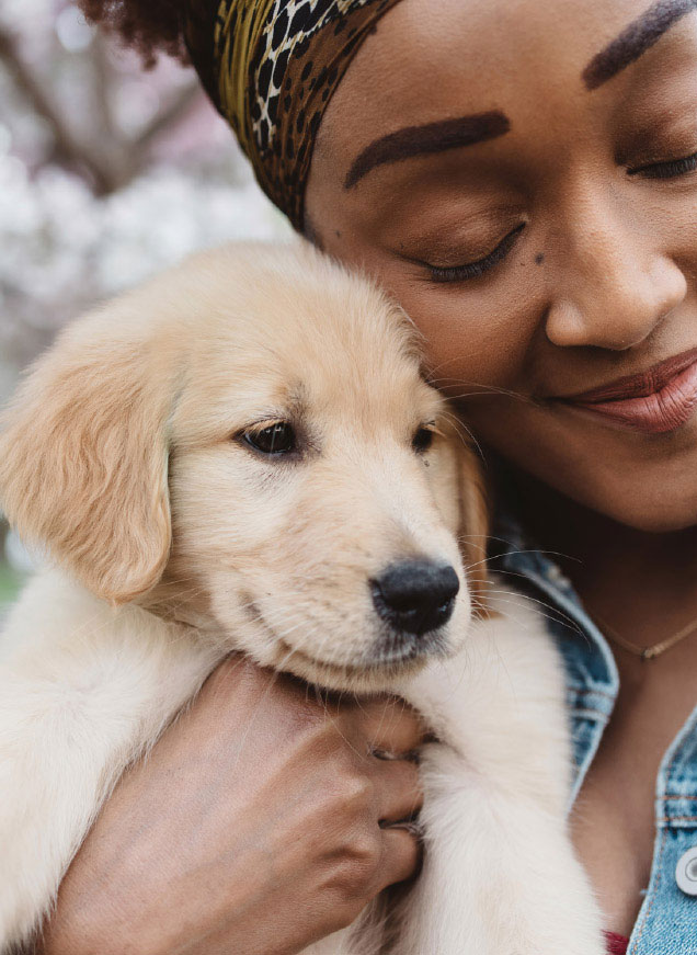 a smiling woman with her eyes closed cuddling a puppy outside